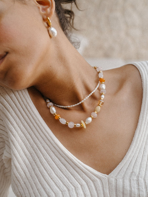 Zarte PURELEI Kette mit Muscheln und Perlen, getragen mit goldenen Creolen, elegante Stimmung.