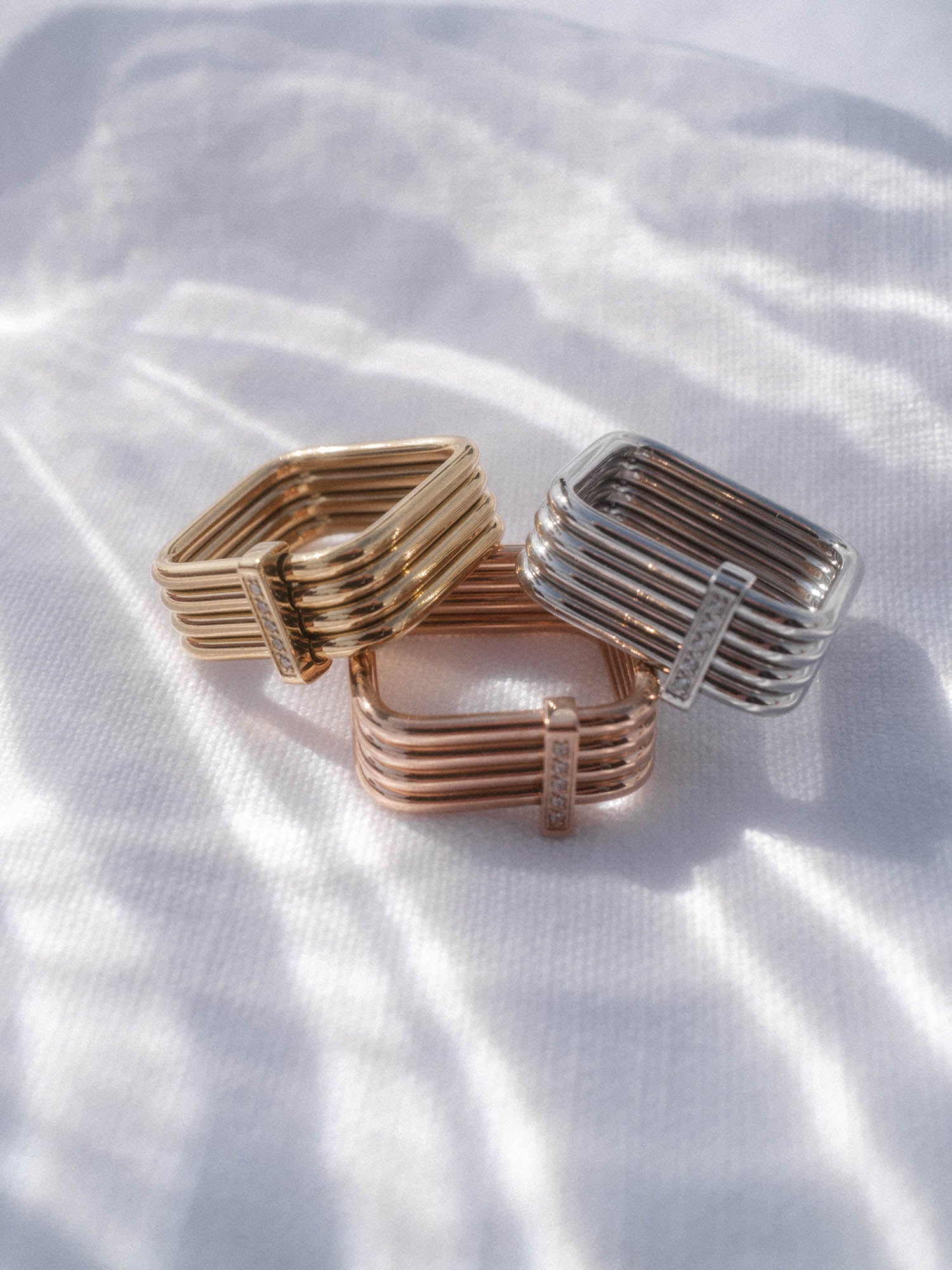 Drei PURELEI Soft Glow Ringe in Gold, Silber und Roségold mit Zirkoniaschliff, sanft im Licht auf hellem Stoff.