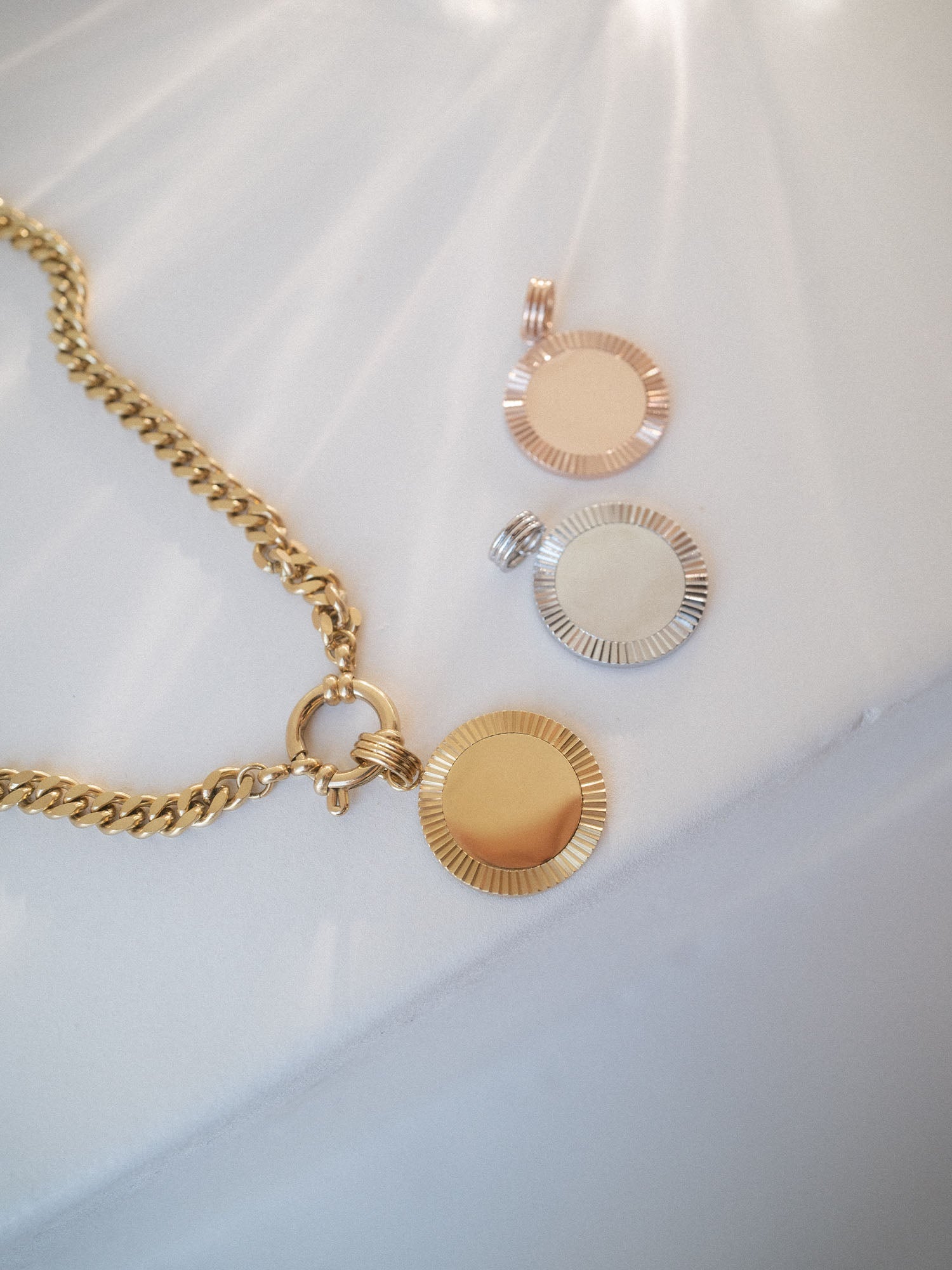 Inner Circle Charm von PURELEI in Gold, Silber und Roségold mit geriffeltem Sonnenmotiv, elegant auf hellem Hintergrund.